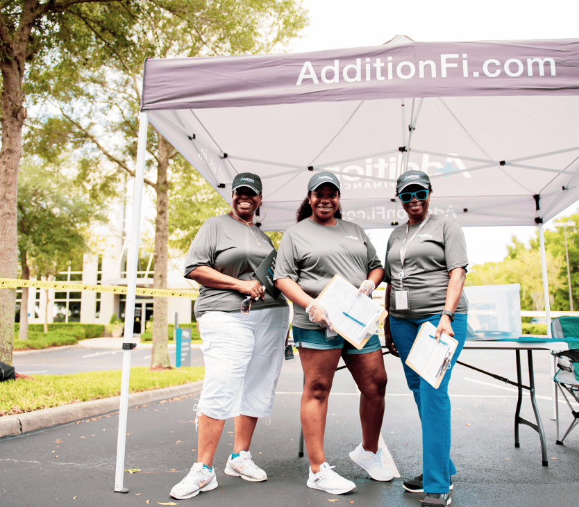 3 women in front of an outside Addition information tent