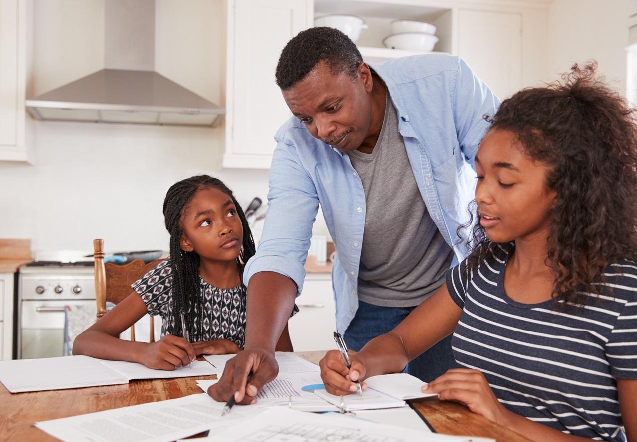 A father helping his two children with homework in the kitchen