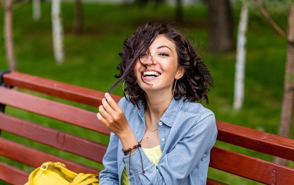 Woman playing with hair and sitting on a park bench