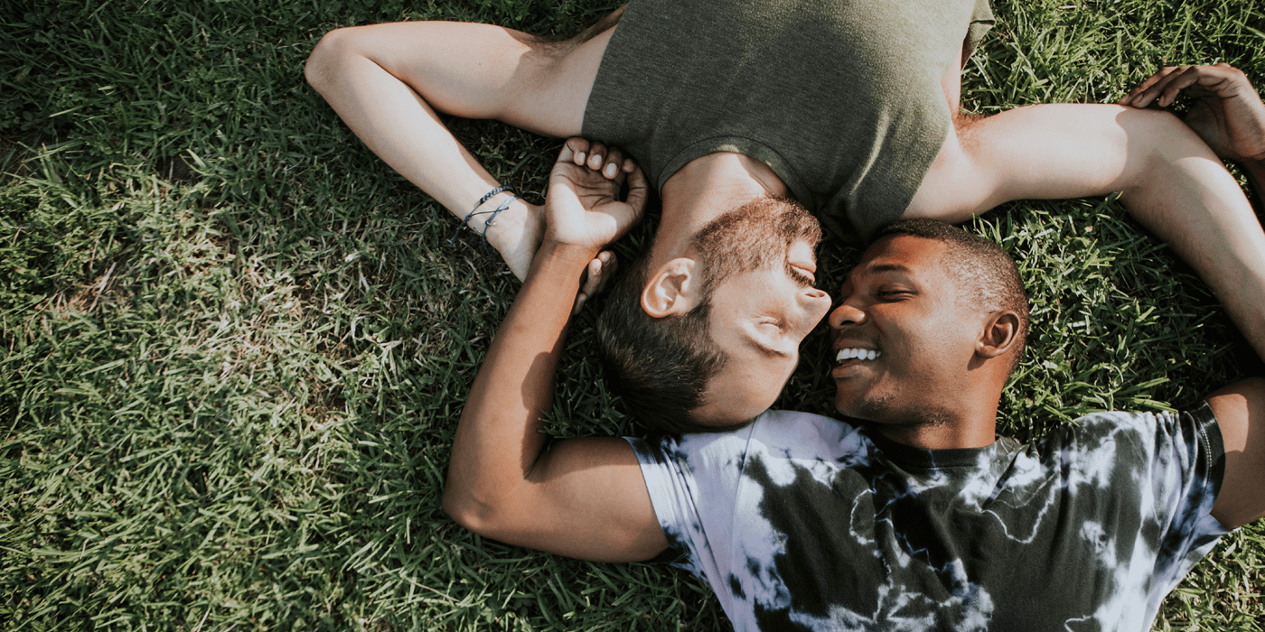 Two men laying down on the grass smiling at each other.