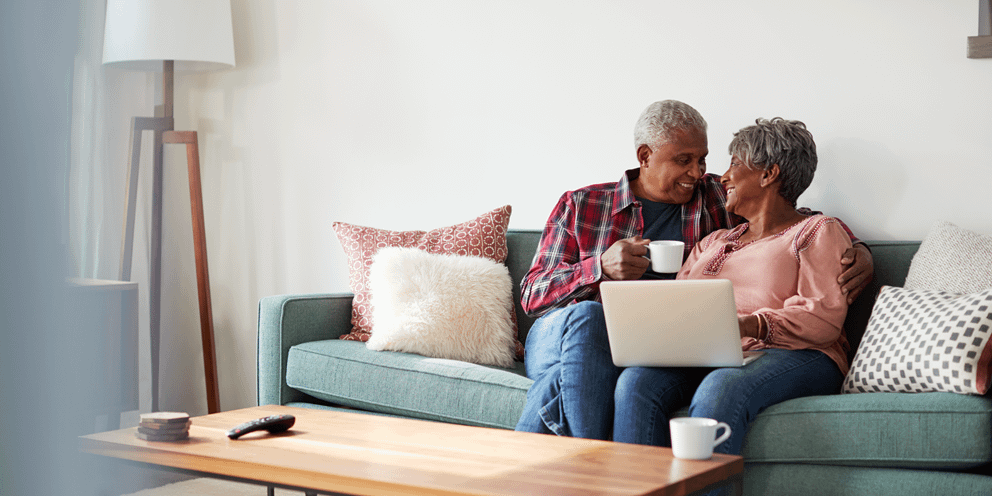 Older couple smiling at each other sitting on the couch.